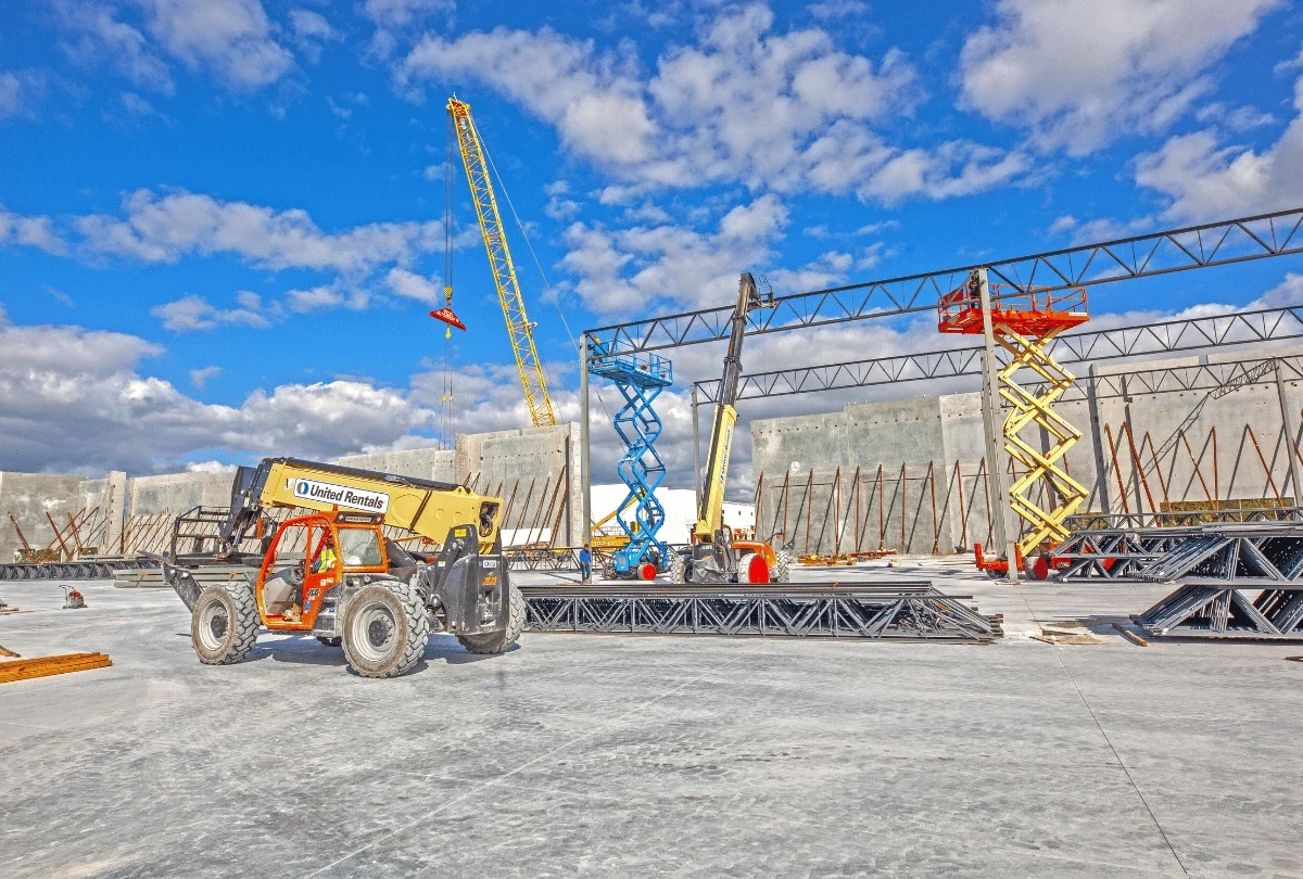 Active industrial construction site with a crane, lift, and structural beams.
